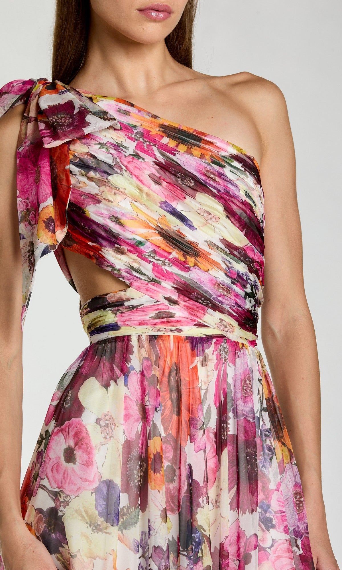Woman wearing the Mac Duggal 68553 long formal dress, featuring a one-shoulder A-line silhouette, floral-print pleated semi-sheer skirt, and waist cut-out detail.